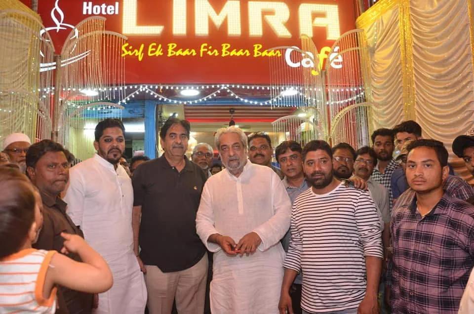 A group of people standing in front of the lit Hotel Limra Café signboard reading 'Sirf Ek Baar Fir Baar Baar'
